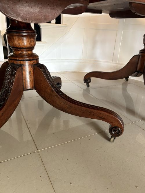fig 1. A polished Regency mahogany dining table featuring a three-pillar pedestal base with splayed reeded legs ending in brass castors.