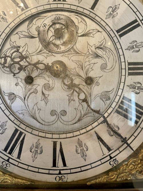 fig 2. A George III oak longcase clock featuring an etched brass dial with silvered chapter ring, inlaid wood motif pediment, and an arched trunk door.