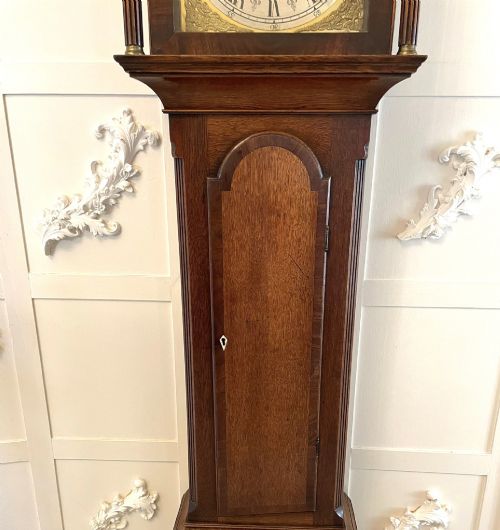fig 3. A George III oak longcase clock featuring an etched brass dial with silvered chapter ring, inlaid wood motif pediment, and an arched trunk door.