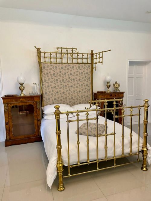 fig 4. An antique Victorian solid brass half tester double bed featuring turned posts, spindle balusters, cast decorative mounts, and an upholstered floral panel.