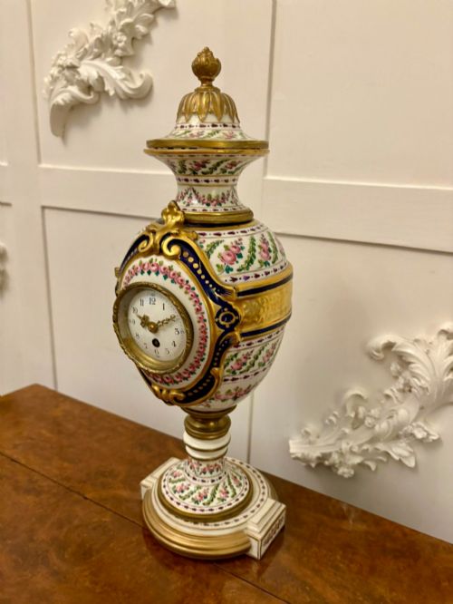 fig 3. A French hand-painted porcelain urn-shaped mantel clock featuring gold leaf accents, cobalt blue borders, and pink floral garlands on a gilded pedestal base.