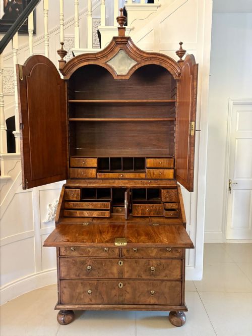 An antique Queen Anne burr walnut bureau bookcase featuring a double-domed cresting with urn finials, double mirrored doors, a sloping fall-front desk section, and a chest of drawers on bun feet. View II