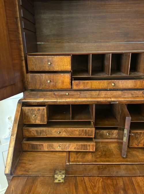 An antique Queen Anne burr walnut bureau bookcase featuring a double-domed cresting with urn finials, double mirrored doors, a sloping fall-front desk section, and a chest of drawers on bun feet. View III