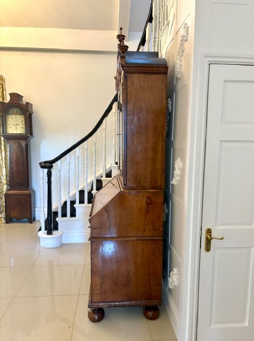 An antique Queen Anne burr walnut bureau bookcase featuring a double-domed cresting with urn finials, double mirrored doors, a sloping fall-front desk section, and a chest of drawers on bun feet. View IV