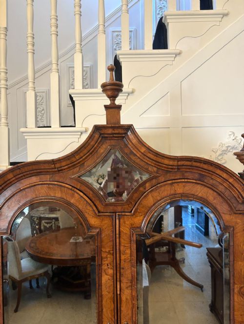 An antique Queen Anne burr walnut bureau bookcase featuring a double-domed cresting with urn finials, double mirrored doors, a sloping fall-front desk section, and a chest of drawers on bun feet. View V