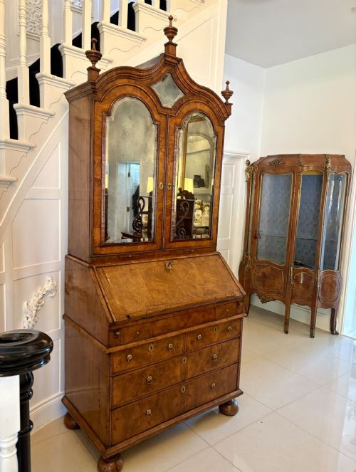 An antique Queen Anne burr walnut bureau bookcase featuring a double-domed cresting with urn finials, double mirrored doors, a sloping fall-front desk section, and a chest of drawers on bun feet. View VII