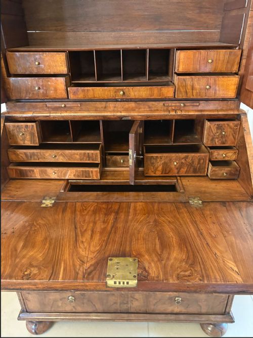 An antique Queen Anne burr walnut bureau bookcase featuring a double-domed cresting with urn finials, double mirrored doors, a sloping fall-front desk section, and a chest of drawers on bun feet. View VIII