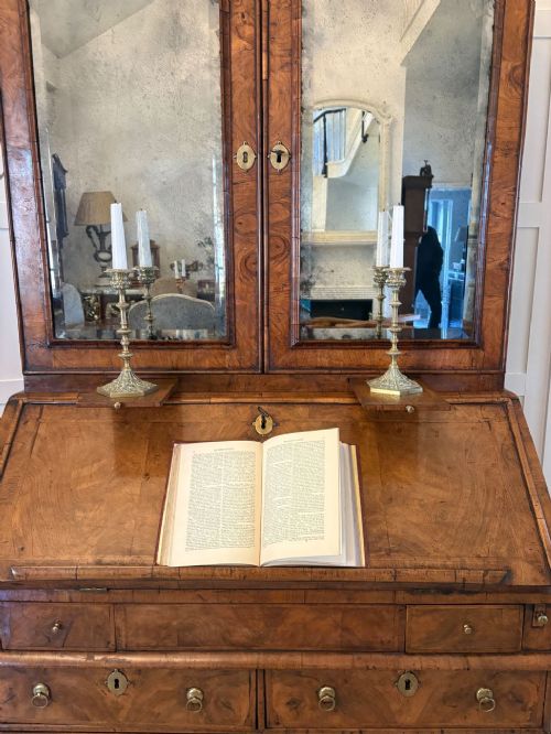 An antique Queen Anne burr walnut bureau bookcase featuring a double-domed cresting with urn finials, double mirrored doors, a sloping fall-front desk section, and a chest of drawers on bun feet. View IX