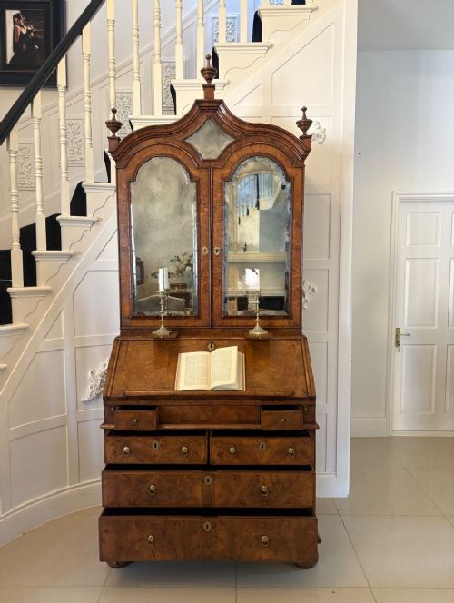 An antique Queen Anne burr walnut bureau bookcase featuring a double-domed cresting with urn finials, double mirrored doors, a sloping fall-front desk section, and a chest of drawers on bun feet. View X