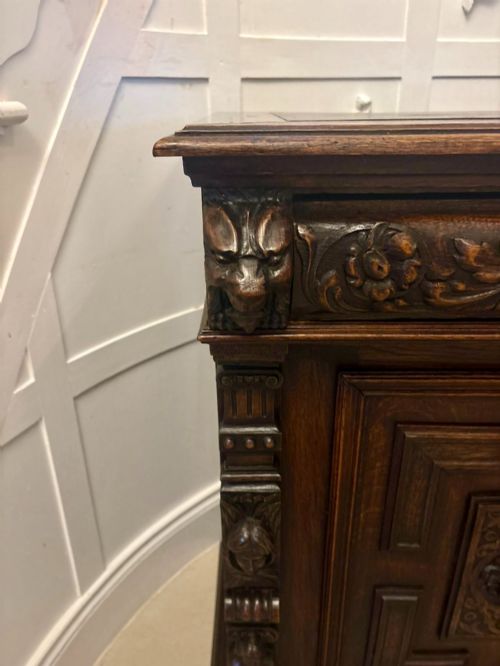 fig 1. A dark carved oak sideboard featuring geometric panelled cupboard doors with central lion mask carvings and a detailed relief frieze.