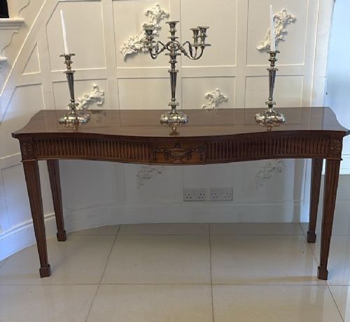 A pair of polished mahogany serpentine-front console tables featuring fluted aprons, carved central urn motifs, and tapered fluted legs. View XIV