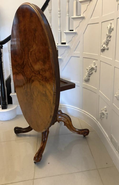 An antique Victorian oval tilt-top dining table featuring book-matched burr walnut grain mounted on a carved central column and tripod base with castors. View XIV