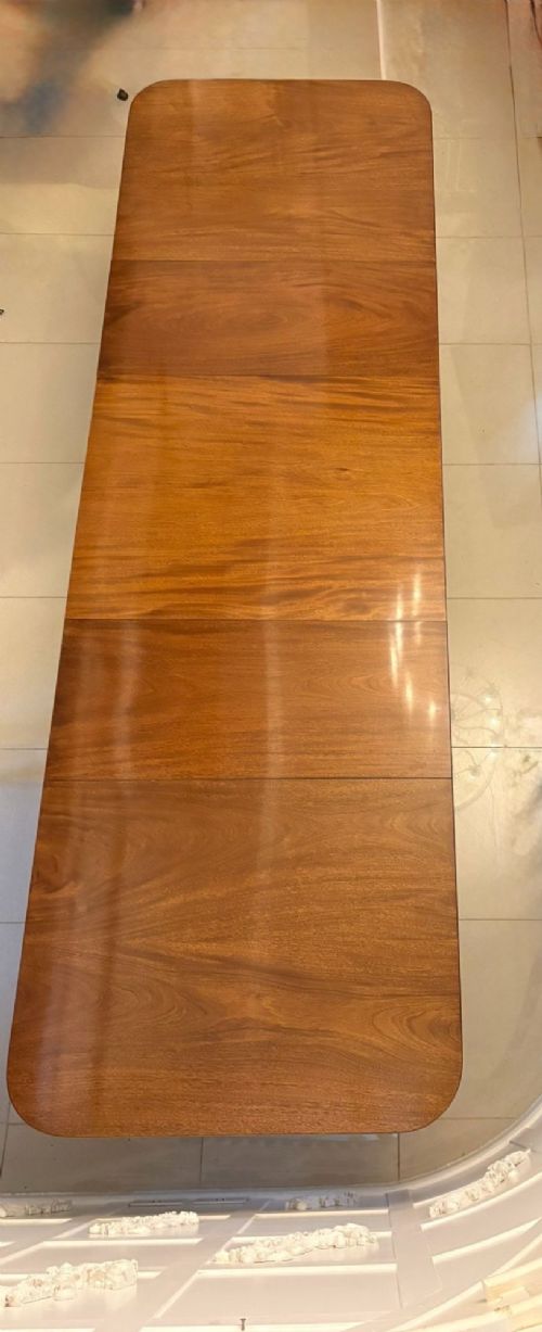 fig 1. An extended mahogany dining table featuring a highly polished figured timber top supported by a three-pillar pedestal base with splayed legs and brass castors.