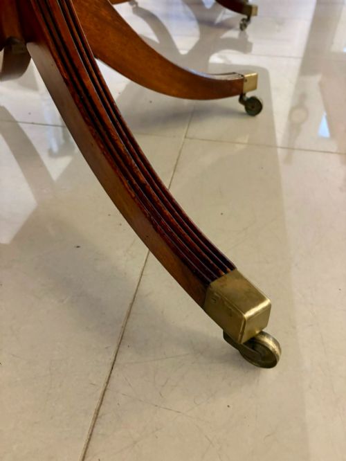 fig 2. An extended mahogany dining table featuring a highly polished figured timber top supported by a three-pillar pedestal base with splayed legs and brass castors.