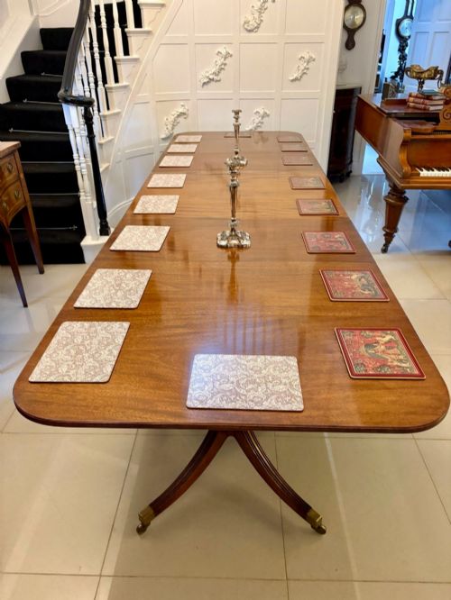 fig 3. An extended mahogany dining table featuring a highly polished figured timber top supported by a three-pillar pedestal base with splayed legs and brass castors.