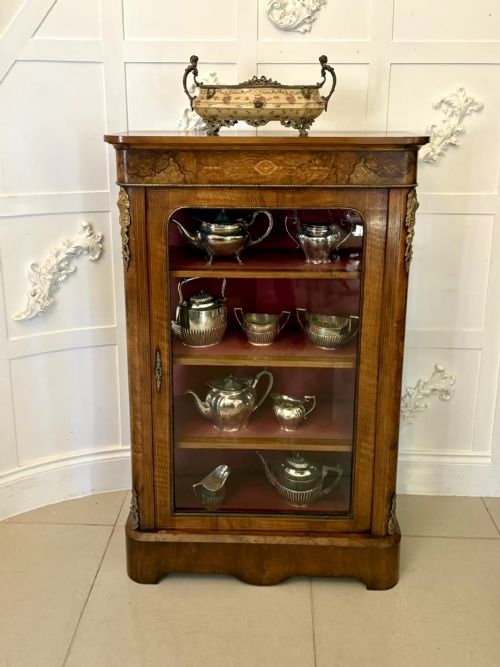 fig 2. A Victorian burr walnut pier cabinet featuring a single glazed door, floral marquetry along the frieze, and gilt ormolu corner mounts.
