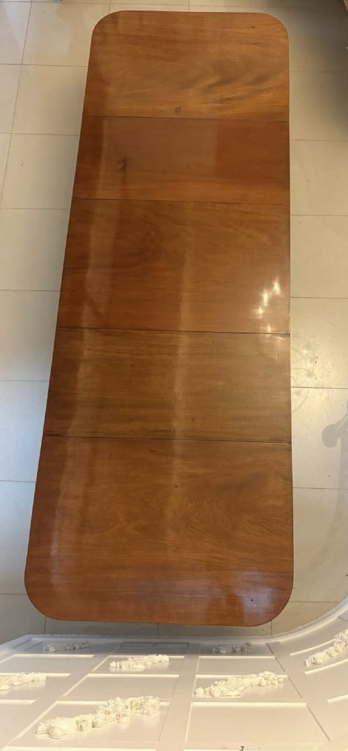 fig 3. A large Georgian extending dining table crafted from polished figured mahogany with a three-pillar tripod pedestal base and brass castors.