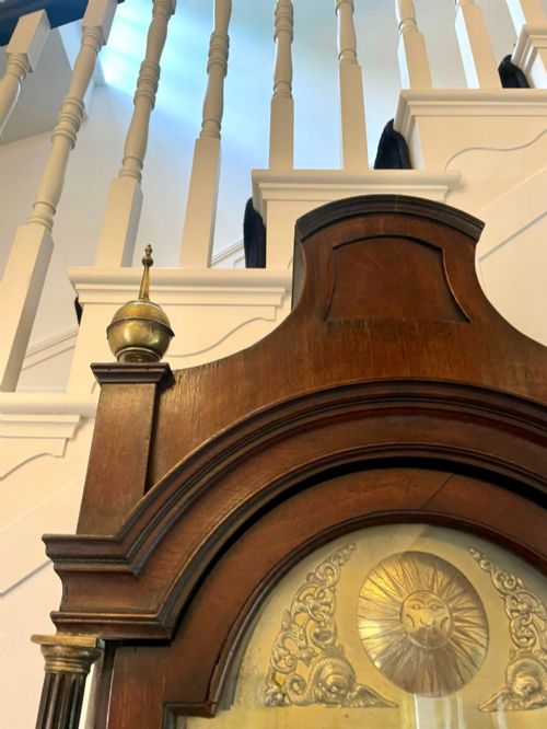 fig 2. A George III mahogany longcase clock featuring an arched brass dial, urn finials, and an arched trunk door.
