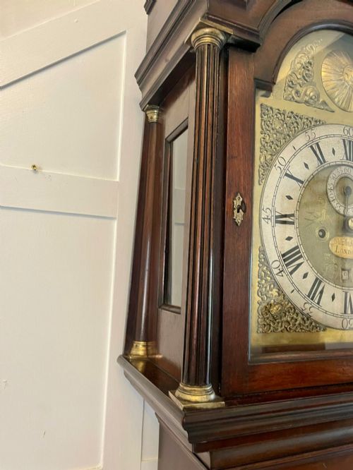 fig 4. A George III mahogany longcase clock featuring an arched brass dial, urn finials, and an arched trunk door.