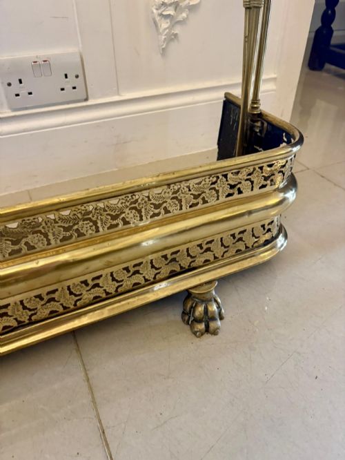fig 1. An antique Regency period brass fireplace fender featuring intricate pierced metalwork, claw feet, and matching original brass fire irons positioned at either end.