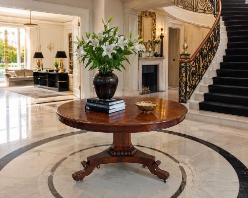 fig 1. A circular Regency tilt-top centre table featuring highly figured flame mahogany veneers, shown in the upright position on a scrolled pedestal base with brass castors.