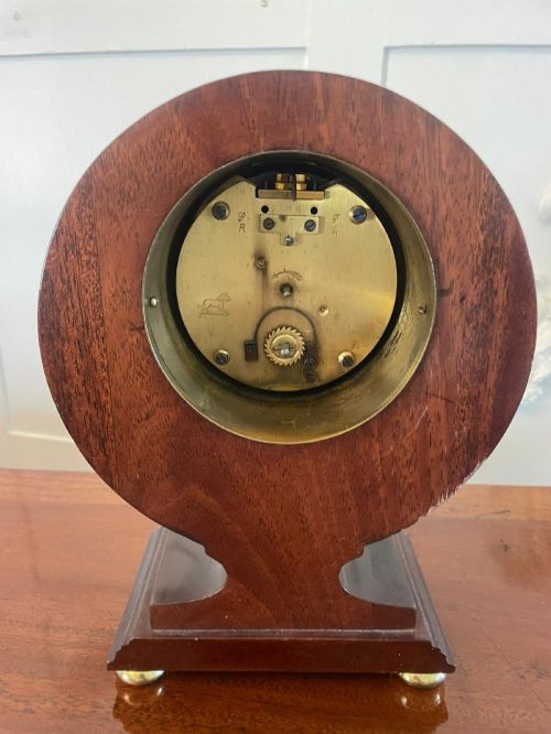 fig 1. An Edwardian mahogany mantle clock featuring floral satinwood inlay, a white dial with Roman numerals, a brass bezel, and small brass bun feet.