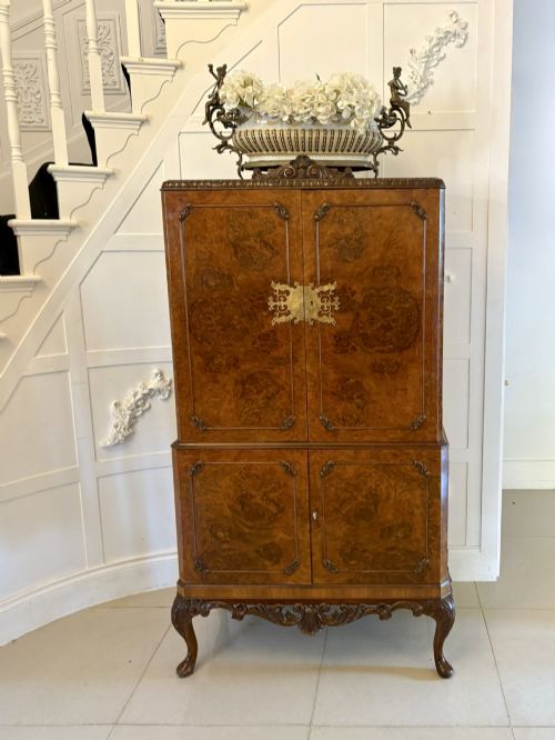 fig 1. An antique burr walnut cocktail cabinet featuring two upper doors with ornate brass hardware, set on carved cabriole legs.