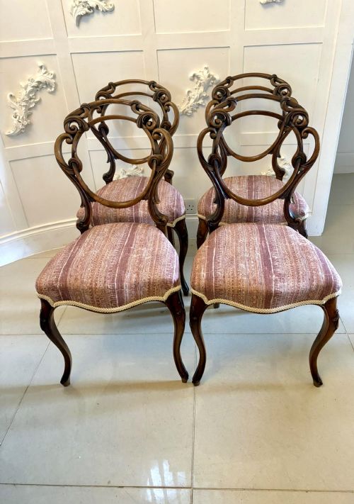 fig 1. A set of four Victorian walnut balloon back dining chairs featuring carved openwork backrests, cabriole front legs, and patterned rose-coloured upholstered seats.