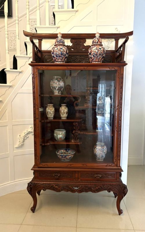 fig 1. A carved reddish-brown hardwood display cabinet featuring a pagoda cresting, glass door, asymmetrical interior shelves, lower drawers, and cabriole legs.