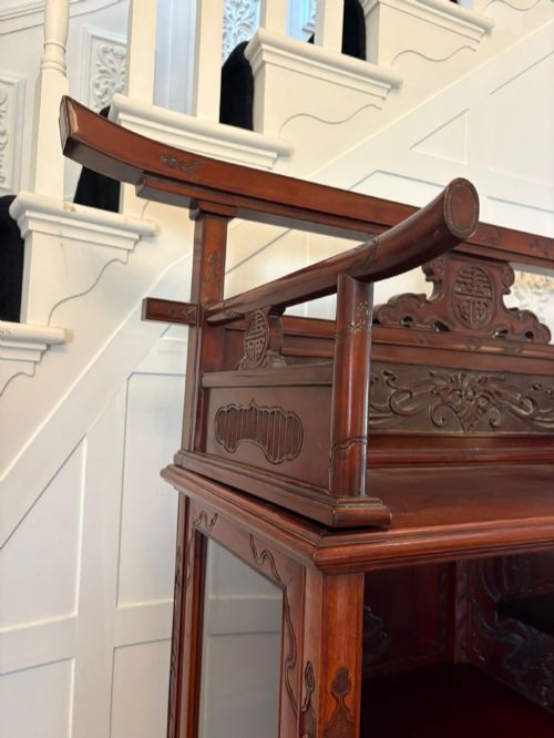 fig 4. A carved reddish-brown hardwood display cabinet featuring a pagoda cresting, glass door, asymmetrical interior shelves, lower drawers, and cabriole legs.