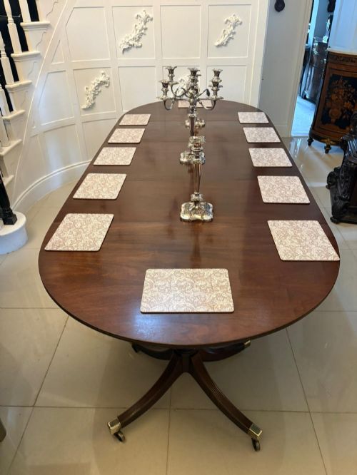 fig 2. A large mahogany extending dining table featuring an oval surface with two additional leaves, supported by splayed pedestal legs with brass castors.