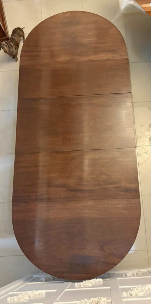 fig 3. A large mahogany extending dining table featuring an oval surface with two additional leaves, supported by splayed pedestal legs with brass castors.