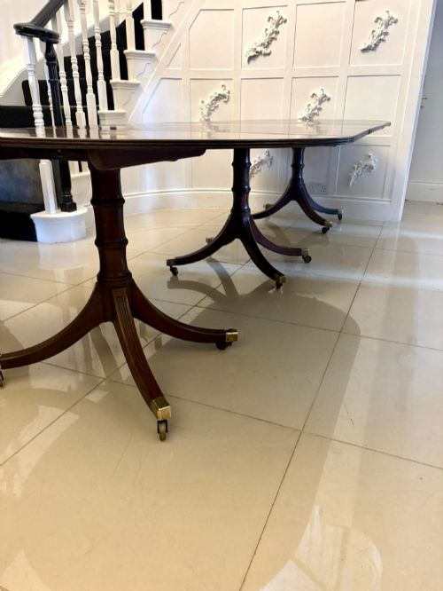 fig 4. A large mahogany extending dining table featuring an oval surface with two additional leaves, supported by splayed pedestal legs with brass castors.