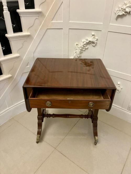 fig 1. A Regency period mahogany sofa table featuring two drop-leaf sides, a single drawer with brass ring handles, reeded splayed legs, a turned stretcher bar, and brass castors.