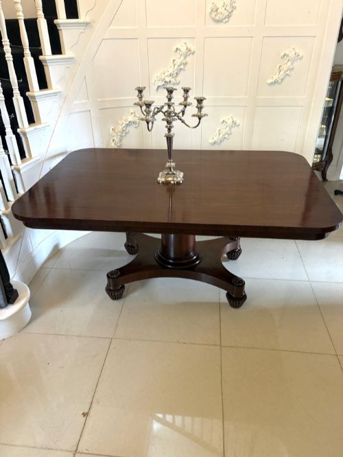 fig 2. A William IV figured mahogany tilt top dining table shown upright, featuring rounded corners, a smooth grain finish, and a central pedestal base with carved feet.