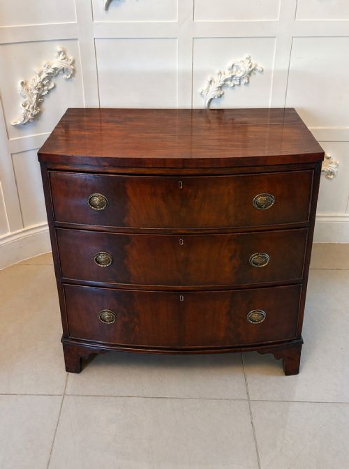 fig 2. A Georgian mahogany bow-front chest of three drawers featuring oval brass drop handles and raised on bracket feet.