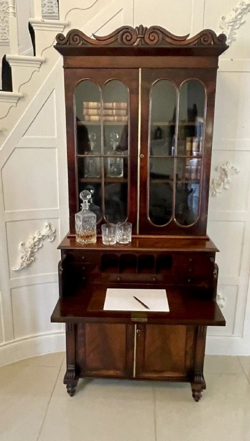 An antique Regency mahogany secretaire bookcase featuring a carved scroll pediment, glazed upper doors, a fall-front desk drawer, and a lower two-door cupboard. View II