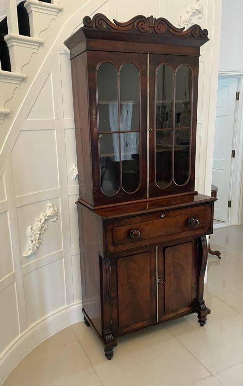 An antique Regency mahogany secretaire bookcase featuring a carved scroll pediment, glazed upper doors, a fall-front desk drawer, and a lower two-door cupboard. View XI