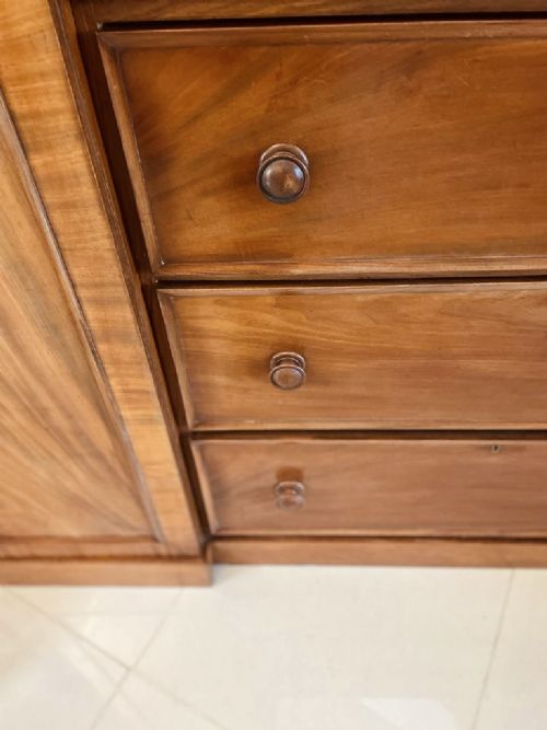 A William IV mahogany breakfront wardrobe featuring two tall outer cupboards flanking a central chest of three drawers with a carved gallery back. View VII