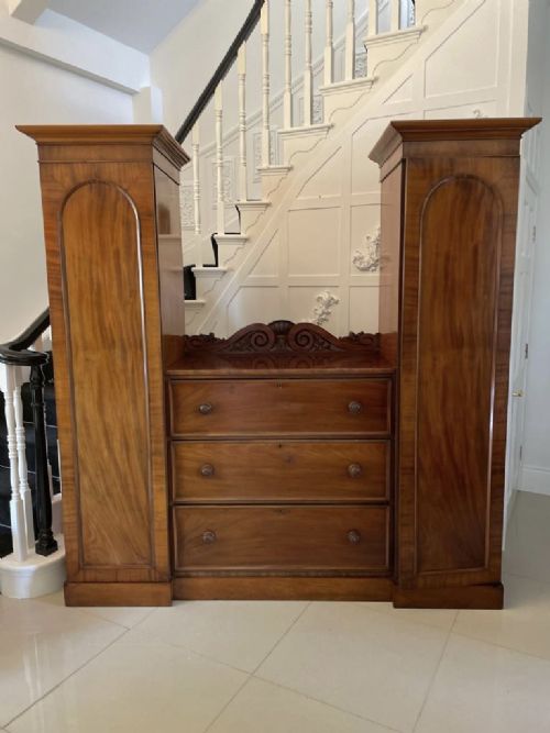 A William IV mahogany breakfront wardrobe featuring two tall outer cupboards flanking a central chest of three drawers with a carved gallery back. View XII