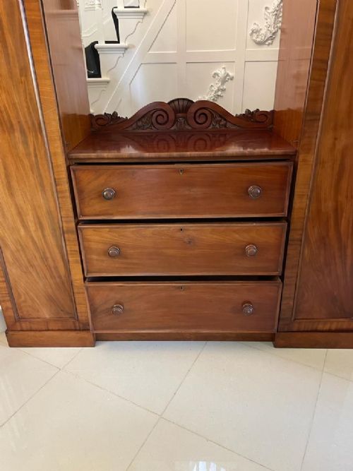 A William IV mahogany breakfront wardrobe featuring two tall outer cupboards flanking a central chest of three drawers with a carved gallery back. View XIII