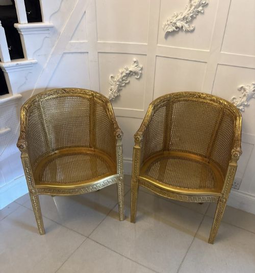 fig 3. A pair of French Louis XVI style carved giltwood tub armchairs featuring curved caned backs and dark blue velvet seat cushions.