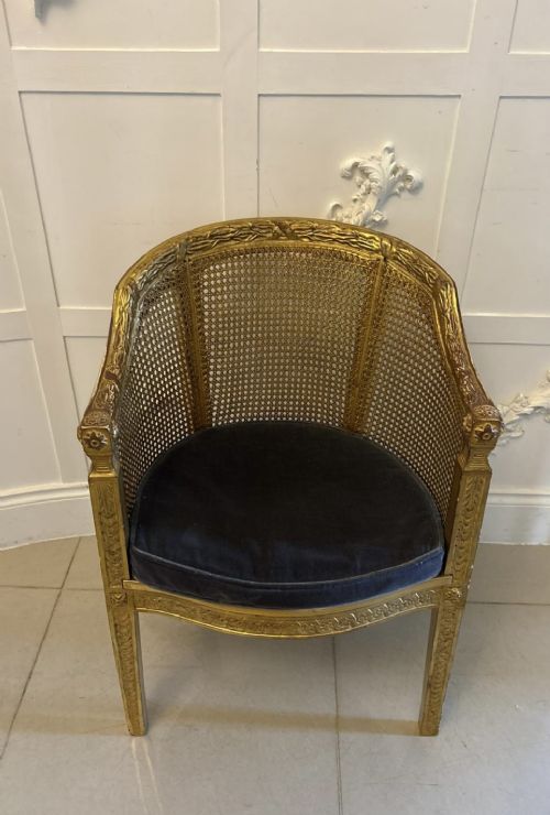 A pair of French Louis XVI style carved giltwood tub armchairs featuring curved caned backs and dark blue velvet seat cushions. View X