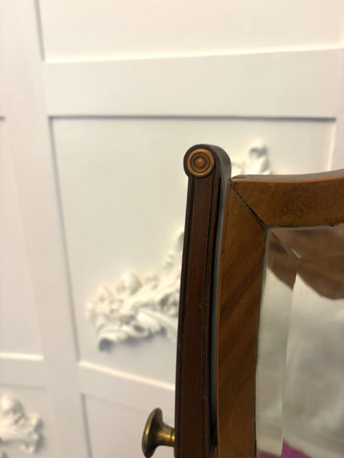 fig 4. An Edwardian mahogany toilet mirror featuring a shield-shaped frame with bevelled glass mounted on a swivelling stand with brass knobs.