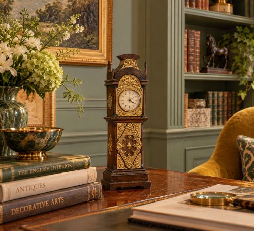 fig 2. A dark oak miniature grandfather table clock with ornate embossed brass panels and a white dial featuring Roman numerals.