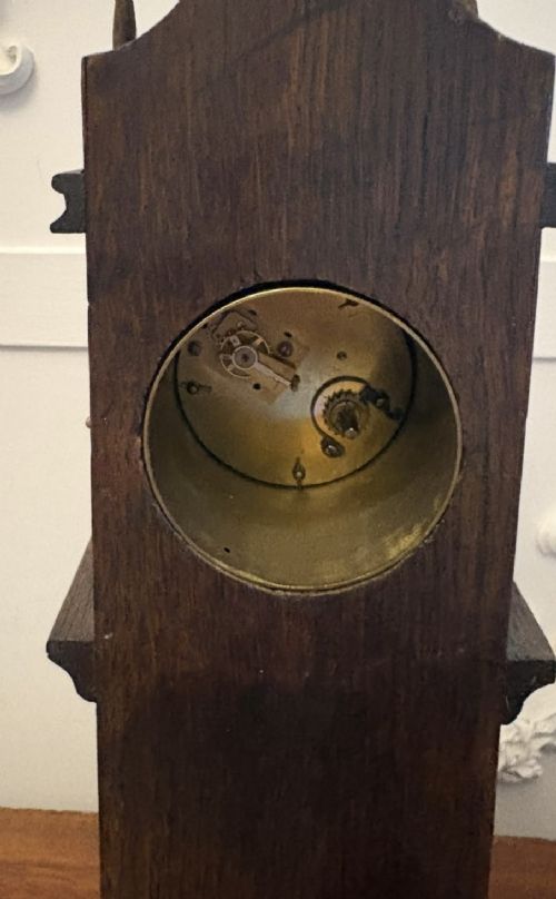 fig 4. A dark oak miniature grandfather table clock with ornate embossed brass panels and a white dial featuring Roman numerals.