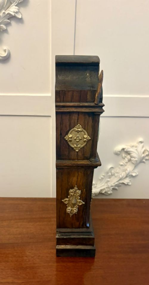 fig 6. A dark oak miniature grandfather table clock with ornate embossed brass panels and a white dial featuring Roman numerals.