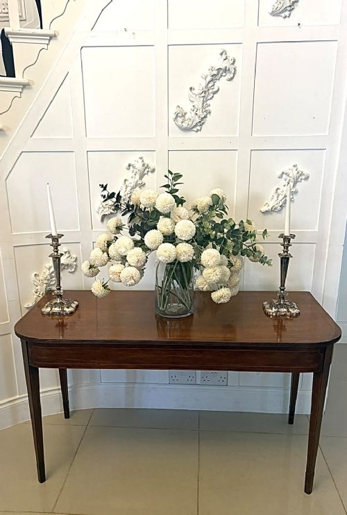 A pair of Georgian mahogany console tables featuring rounded corners, inlaid aprons, and slender tapered legs. View X