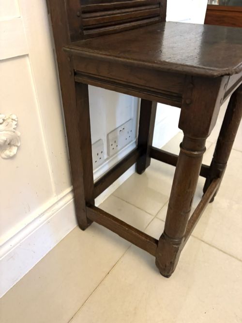 fig 1. A dark oak 17th-century correction chair featuring a tall panelled backrest, carved crest rail with small wooden finials, solid wooden seat, turned front legs, and plain stretchers.