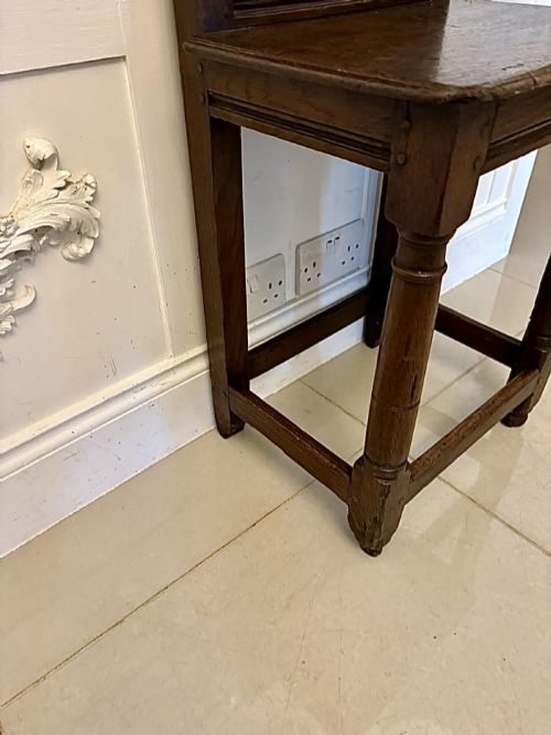 fig 2. A dark oak 17th-century correction chair featuring a tall panelled backrest, carved crest rail with small wooden finials, solid wooden seat, turned front legs, and plain stretchers.